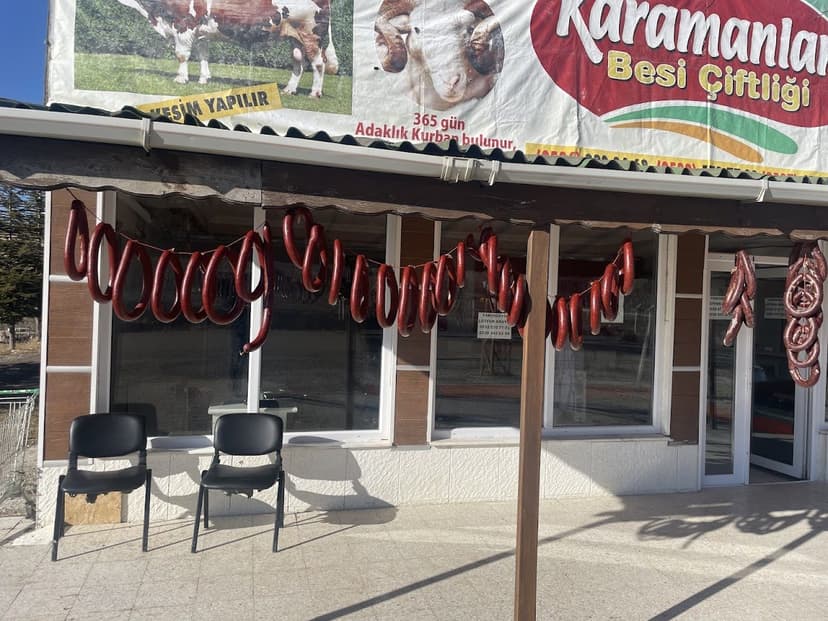 Karamanlar Et dükkân önü — asılı ev yapımı sucuklar ve Karamanlar Besi Çiftliği tabelası
