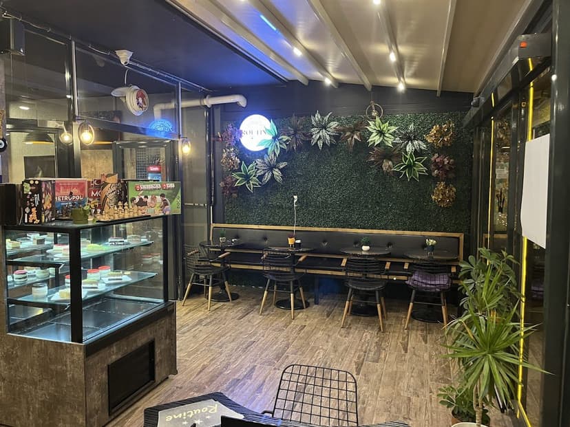 Routine Game Cafe iç mekan — yeşil duvar, oturma alanı ve tatlı dolabı