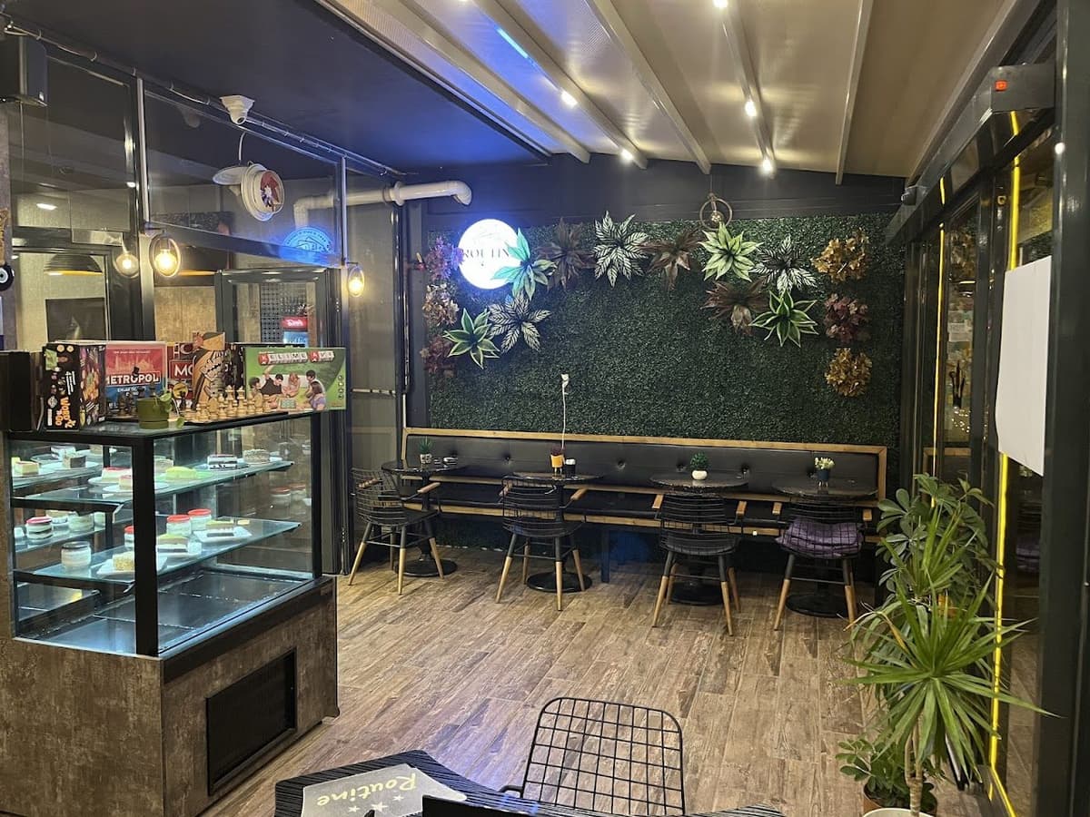 Routine Game Cafe iç mekan — yeşil duvar, oturma alanı ve tatlı dolabı